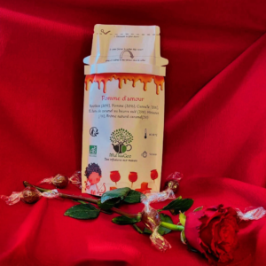 Une infusion à la pomme, cannelle, hibiscus et caramel présentée avec une rose et des caramel beurre salé sur fond rouge.